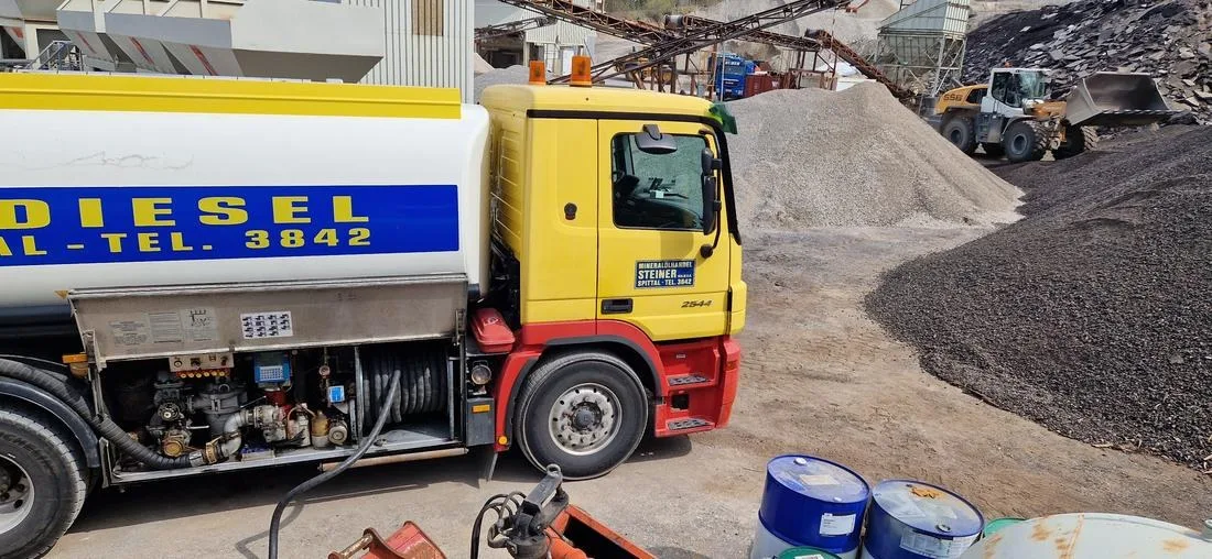 Gelber Tankwagen mit der Aufschrift Diesel betankt im Schotterwerk, dahinter ein Radlader